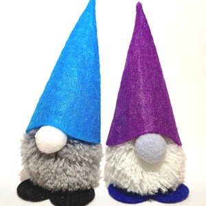 May include: Two handmade gnome figurines. One gnome has a blue felt hat, gray beard, white nose, and black shoes. The other gnome has a purple felt hat, white beard, gray nose, and blue shoes. Both are on a white background.