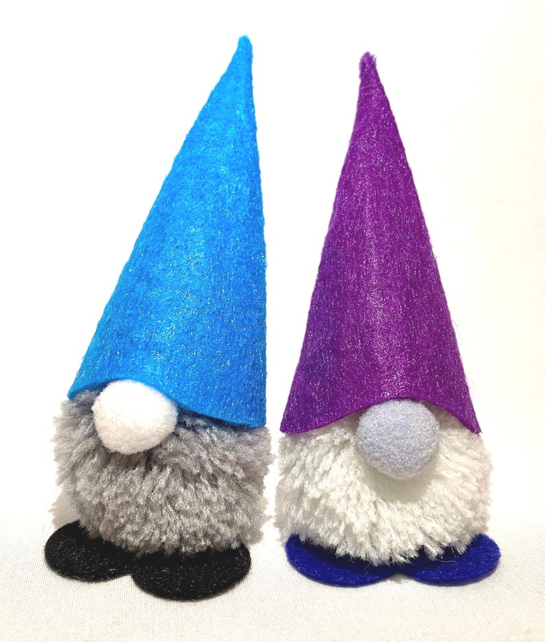 May include: Two handmade gnome figurines. One gnome has a blue felt hat, gray beard, white nose, and black shoes. The other gnome has a purple felt hat, white beard, gray nose, and blue shoes. Both are on a white background.