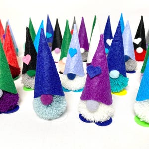 May include: A collection of colorful gnome figurines with felt cone hats in various colors, including blue, green, red, and purple. Each gnome has a fluffy beard and a small pom-pom nose. Some have heart-shaped accents.