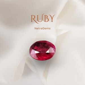 May include: A faceted, oval-cut ruby gemstone with a deep red hue, set against a white fabric background. The word "RUBY" is displayed in a stylized font above the gemstone, with the text "NetraGems" below.