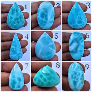 May include: Nine polished larimar gemstones in various shapes, including teardrop and oval. The stones display a range of blue hues with white veining, resembling ocean waves. Each stone is unique, showcasing natural patterns and textures.