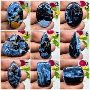 Può includere: Nove pietre preziose di Pietersite lucidata in varie forme. Le pietre mostrano un mix di colori blu, nero e oro con motivi a vortice unici. Ogni pietra è tenuta in una mano, mostrando la bellezza naturale e le variazioni delle pietre.