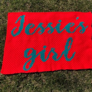 May include: A red crocheted blanket with the words "Jessie's girl" in teal.