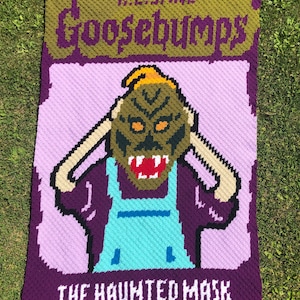 Könnte beinhalten: Eine gehäkelte Decke mit dem Goosebumps-Buchcover für "The Haunted Mask". Das Cover zeigt einen violetten Hintergrund mit einer Comicfigur, die eine grüne Maske und ein blaues Hemd trägt. Der Titel "Goosebumps" ist in grün und violetter Schrift, und der Buchtitel "The Haunted Mask" ist in weißer Schrift.