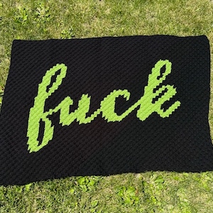 Puede incluir: Manta negra con la palabra "fuck" en letras cursivas de color verde brillante. La manta está sobre hierba verde.