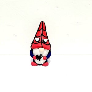 Puede incluir: Una figura de gnomo roja y azul con barba blanca y un sombrero de telaraña. El gnomo sostiene una araña negra en sus manos.