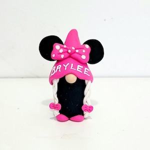 May include: A pink and black gnome figurine with a bow and the name "Brylee" written on the hat.