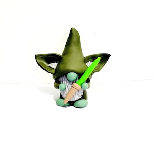 May include: A green gnome figurine with a white beard holding a green carrot in its hands.