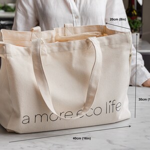May include: A large, off-white canvas tote bag with the text "a more eco life" printed on the front. The bag measures 16 inches wide, 12 inches tall, and 8 inches deep.