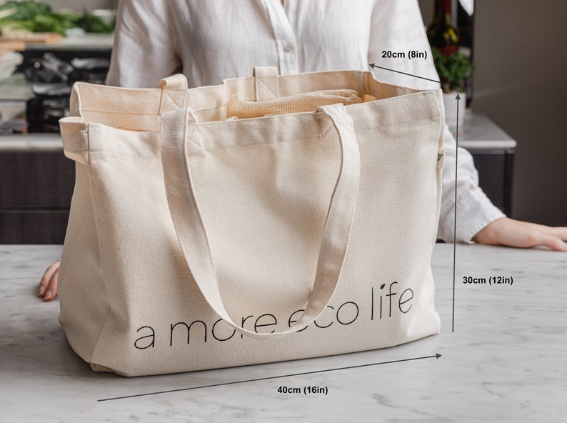 May include: A large, off-white canvas tote bag with the text "a more eco life" printed on the front. The bag measures 16 inches wide, 12 inches tall, and 8 inches deep.