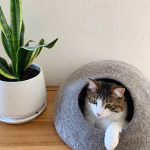 Jimmy inside a light grey medium cave with his paw nonchalently draped over the opening.  The light grey caves are made using a combination of natural wool colours - they are not dyed.