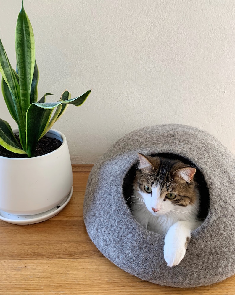 Jimmy inside a light grey medium cave with his paw nonchalently draped over the opening.  The light grey caves are made using a combination of natural wool colours - they are not dyed.
