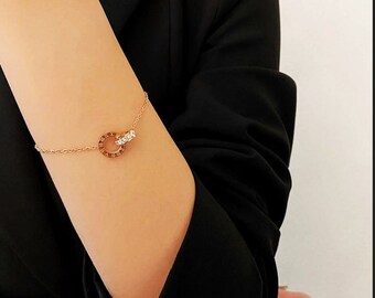 Peut inclure: Un bracelet délicat en chaîne dorée avec un pendentif à double cercle. Un cercle est orné de petites pierres claires, tandis que l'autre présente des chiffres romains.