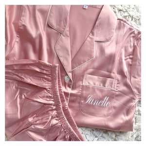 May include: A pink satin pyjama set with white piping and the name "Janelle" embroidered on the pocket.