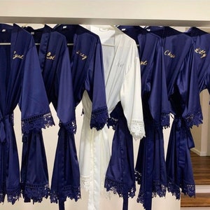 May include: Six satin robes with lace trim, five are navy blue and one is white. The robes have gold lettering with the names "Lynd", "Lol", "Izzy", "Lily", "Chris", and "Kyl" on them.