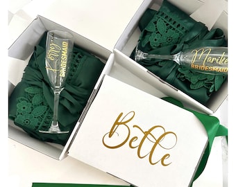 Può includere: Tre scatole regalo bianche con accappatoi di raso verde e flute da champagne all'interno. Le scatole sono etichettate con i nomi "Belle", "Maryke Bridesmaid" e "Jenny Bridesmaid".