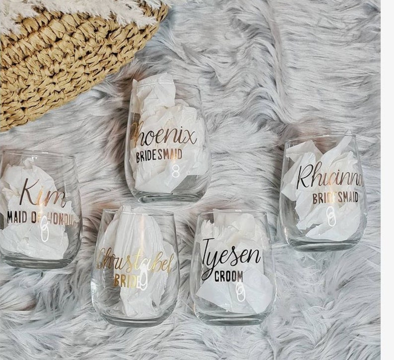 Op de afbeelding: Vijf heldere glazen wijnglazen met gouden letters. De glazen zijn gepersonaliseerd met de namen "Kim Maid of Honor", "Christabel Bride", "Tyesen Groom", "Phoenix Bridesmaid" en "Rhianna Bridesmaid".