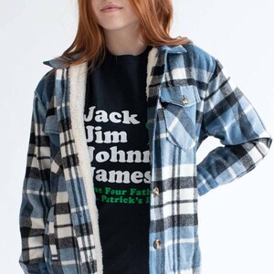 May include: A blue and white plaid flannel shirt with a sherpa lining. The shirt is open and a black t-shirt with the text "Jack Jim John James" is visible underneath.