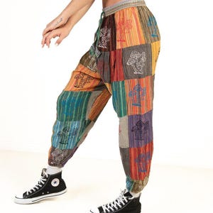 May include: Patchwork pants with a variety of colors and mushroom designs. The pants have a drawstring waist and are worn with black high-top sneakers. The pants are made of a soft, comfortable material.
