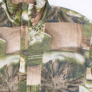 Könnte beinhalten: Ein Hemd mit tropischem Muster. Das Hemd zeigt eine Collage aus Palmen, Blättern und rechteckigen Formen in Grün-, Braun- und Beigetönen. Der Kragen ist sichtbar und der Stoff scheint leicht zu sein. Das Hemd hat ein Knopfdesign.