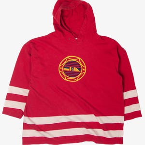Puede incluir: Sudadera con capucha roja con rayas blancas en las mangas y el dobladillo inferior. Un emblema circular con borde dorado y diseño a rayas está centrado en el pecho. La sudadera tiene una capucha con cordón.