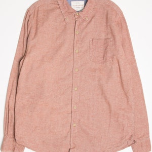May include: A long-sleeved, button-down shirt in a dusty rose color with a small pocket on the left chest. The shirt has a woven texture and a button-down collar.
