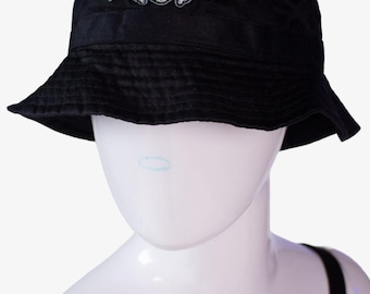 May include: Black bucket hat with the text "STONE COLD" in blue and white, featuring a skull and crossbones design. The hat is displayed on a white mannequin head.