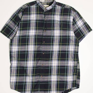 Può includere: Camicia a quadri a maniche corte con chiusura a bottoni e colletto. Il motivo a quadri presenta linee verdi scure, bianche, gialle e blu. La camicia è realizzata in un materiale morbido, probabilmente cotone.