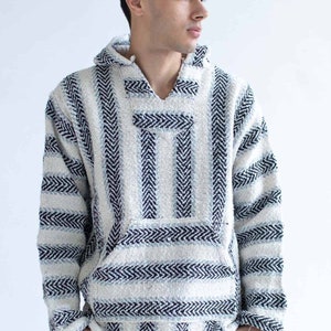 May include: A white and black striped Baja hoodie with a front pocket and hood. The hoodie has a woven texture and a relaxed fit. The design features vertical stripes with a chevron pattern.