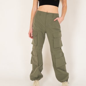 May include: Olive green cargo pants with multiple pockets and a relaxed fit. The pants are paired with a black crop top with a yellow and white trim. Beige sneakers complete the outfit.