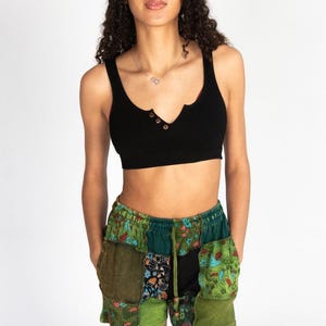 May include: A black ribbed crop top with three buttons and patchwork shorts. The shorts feature various green fabrics with floral and paisley patterns. The shorts have a drawstring waist and pockets.