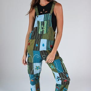 Könnte beinhalten: Patchwork-Latzhose in Grün- und Blautönen mit floralen und Herz-Akzenten. Die Latzhose hat eine Latzvorderseite, verstellbare Träger und Taschen. Die Hose hat eine lockere Passform und ist im Bohemian-Stil gehalten.