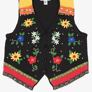 May include: Black knit vest with a V-neck and button closure, adorned with colorful floral embroidery. Features yellow shoulders, red and green trim, and a variety of embroidered flowers in yellow, red, blue, and white.