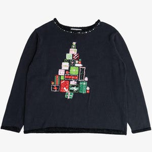 May include: A black long-sleeve jumper featuring a central graphic of a Christmas tree constructed from stacked, colourful gift boxes in shades of red, green, and pink. The neckline is embellished with small silver studs, and the hem has a textured trim.