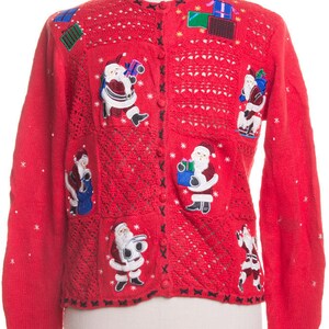 May include: Red Christmas cardigan sweater with Santa Claus and gift box appliqués. The sweater has a button-up front, a round neckline, and a decorative hem. The sleeves are long and the sweater is made of a knit material.