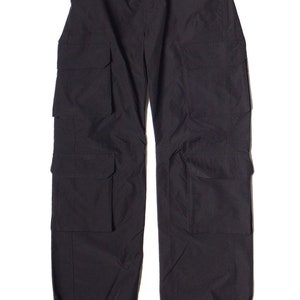 May include: Black cargo pants with multiple pockets on the legs and a button closure at the waist. The pants have a relaxed fit and drawstring cuffs. The fabric appears to be a lightweight material.