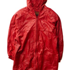 Puede incluir: Chaqueta de cuero rojo brillante con capucha, cierre de cremallera y bolsillos delanteros. La chaqueta larga tiene un cordón en el bajo. El cuero parece ligeramente texturizado.
