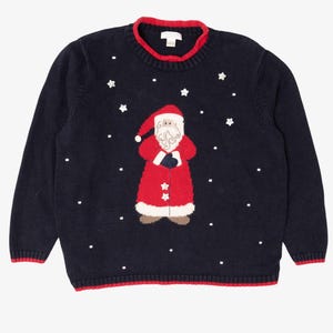 May include: A navy blue long-sleeve knit sweater featuring a central graphic of Santa Claus in a red suit with a white beard. The sweater has a red ribbed crew neckline and hem, decorated with small white embroidered stars and dots throughout.