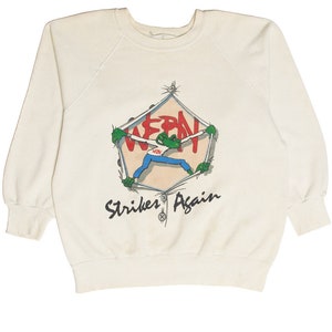 May include: Cream-colored sweatshirt with a graphic of a green frog breaking through a pentagon-shaped frame. The frog wears a blue shirt and the text "WERN" is inside the frame. The words "Strikes Again" are below the frame.