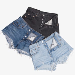 May include: Three pairs of denim shorts in various washes: light blue, medium blue, and black. Each pair features a button fly, classic five-pocket design, and frayed hem. The shorts are arranged on a white background.