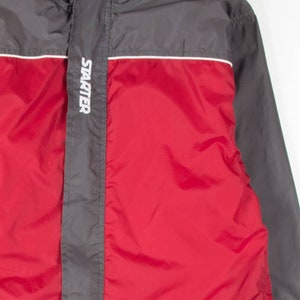 May include: A red and gray Starter jacket. The jacket has a red front panel and gray sleeves and shoulders. The Starter logo is printed in white on the front. A white stripe accents the design. The jacket has a high collar.