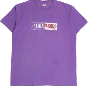Puede incluir: Camiseta de manga corta de color morado con un gráfico rectangular blanco que dice "COMMWORKS FOR WINDOWS" en letras rojas y blancas.