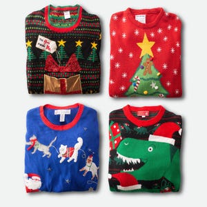 Op de afbeelding: Vier opgevouwen kersttruien. Een zwarte trui met een cadeau- en boomontwerp, een rode trui met een kerstboom en ster, een blauwe trui met katten en een zwarte trui met een dinosaurus met een kerstmuts.