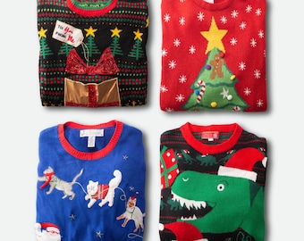 May include: Four folded Christmas sweaters. One black sweater with a gift and tree design, a red sweater with a Christmas tree and star, a blue sweater with cats, and a black sweater with a dinosaur wearing a Santa hat.
