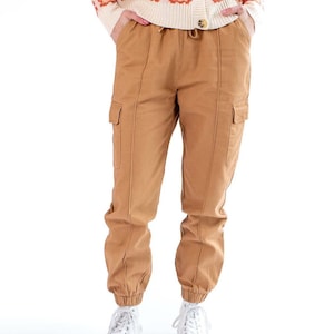 May include: Tan cargo pants with side pockets and a drawstring waist. The pants are paired with white sneakers. A cream-colored cardigan with a floral pattern in shades of pink and orange is also visible.