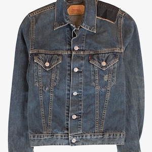 May include: A blue denim jacket with a classic design. Features a button-up front, two chest pockets, and a collar. The jacket has a worn look with a patch on the shoulder. A red and white tag is visible.