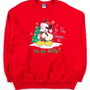 Könnte beinhalten: Roter Weihnachtspullover mit Mickey Mouse, der eine Weihnachtsmütze trägt und einen Sack mit Geschenken hält. Der Text auf dem Pullover lautet "'tis The Season... To Be Jolly!"