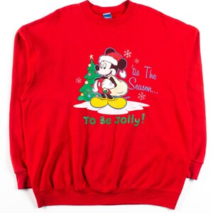 Könnte beinhalten: Roter Weihnachtspullover mit Mickey Mouse, der einen Weihnachtsmann-Hut trägt und einen Sack mit Geschenken trägt. Der Text auf dem Pullover lautet "'tis The Season... To Be Jolly!"