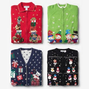 Op de afbeelding: Vier opgevouwen kersttruien. Rode trui met ritssluiting met cadeaus en een teddybeer. Groene trui met ritssluiting met sneeuwpoppen. Marineblauw vest met cadeaus en sneeuwvlokken. Zwarte trui met ritssluiting met sneeuwpoppen en sneeuwvlokken.