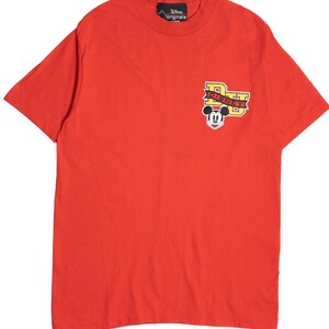 May include: Bright red t-shirt featuring a Mickey Mouse graphic. The graphic includes the word "DISNEY" in yellow and black lettering. The shirt has a crew neck and short sleeves. The Disney Originals logo is on the neck.